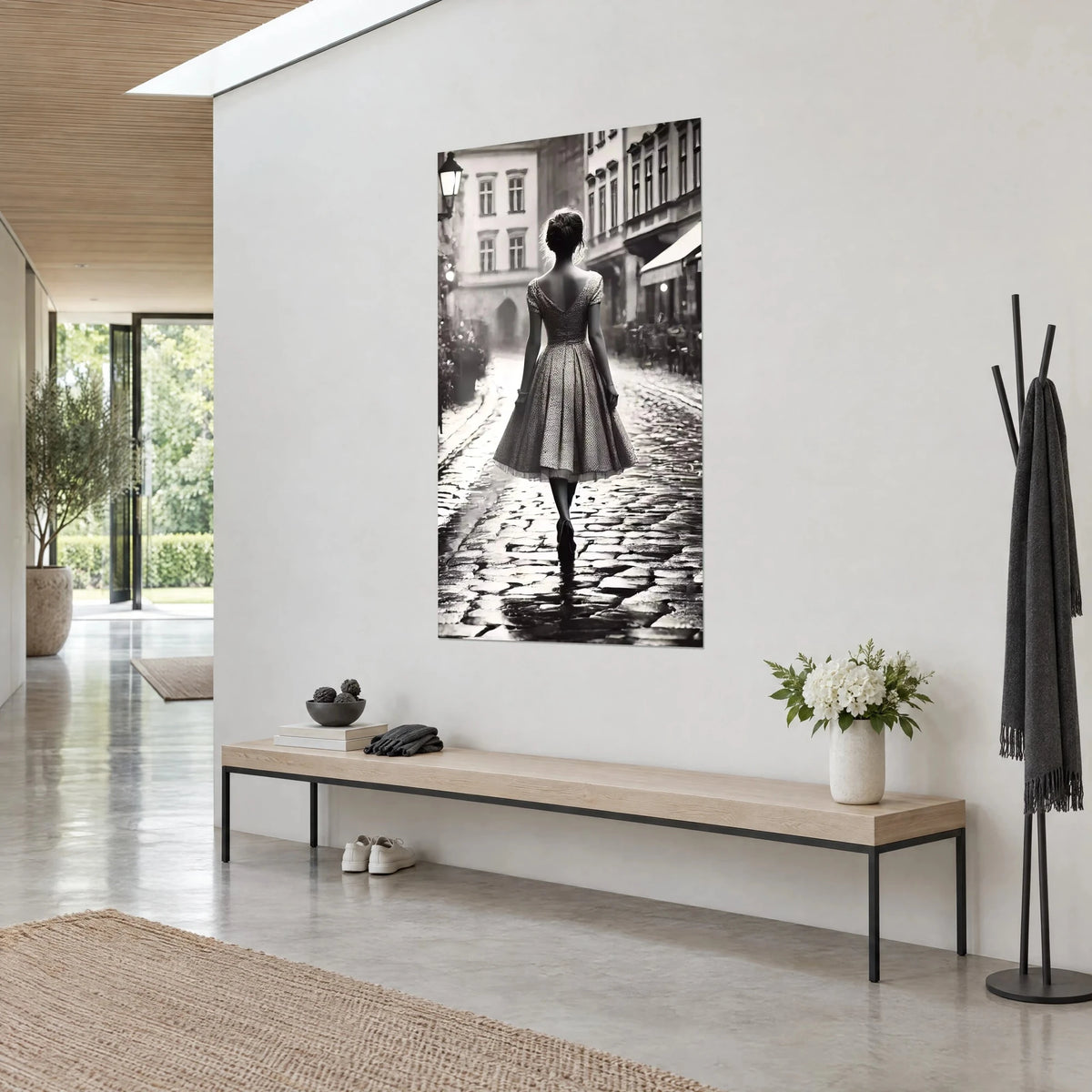 Quadro silhouette femminile in abito plissé, chignon, vicolo di ciottoli grigi e bianchi, su un muro bianco di un corridoio luminoso