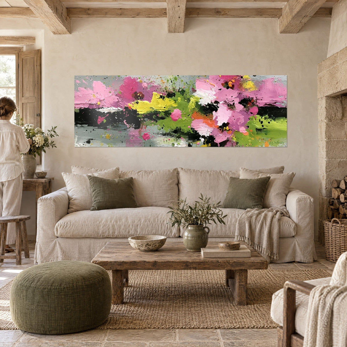 Wall art abstract pink and green flowers, black highlights on silvery grey background, woman seen from behind, above a sofa in a bright living room