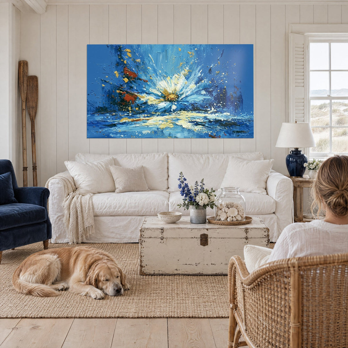 Wall art of a giant daisy in cobalt blue and cream white, gold flecks, above a sofa in a bright living room