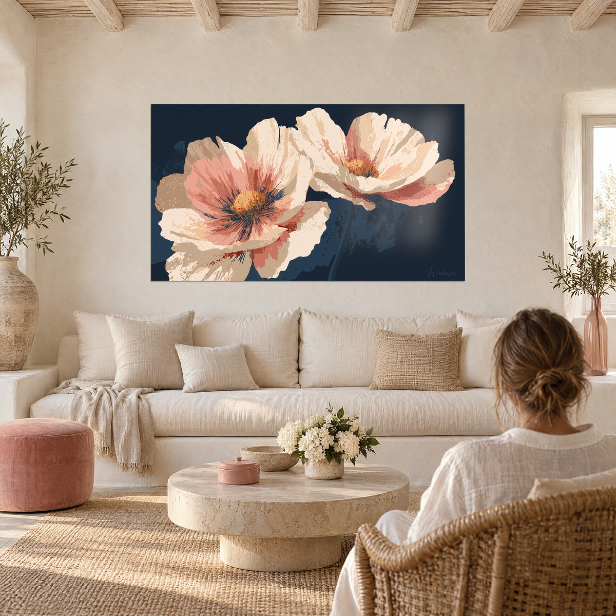 Schilderij crème klaprozen met oranje hartjes op marineblauwe achtergrond, tegenover een vrouw met haar rug naar de kijker, boven een bank in een lichte woonkamer
