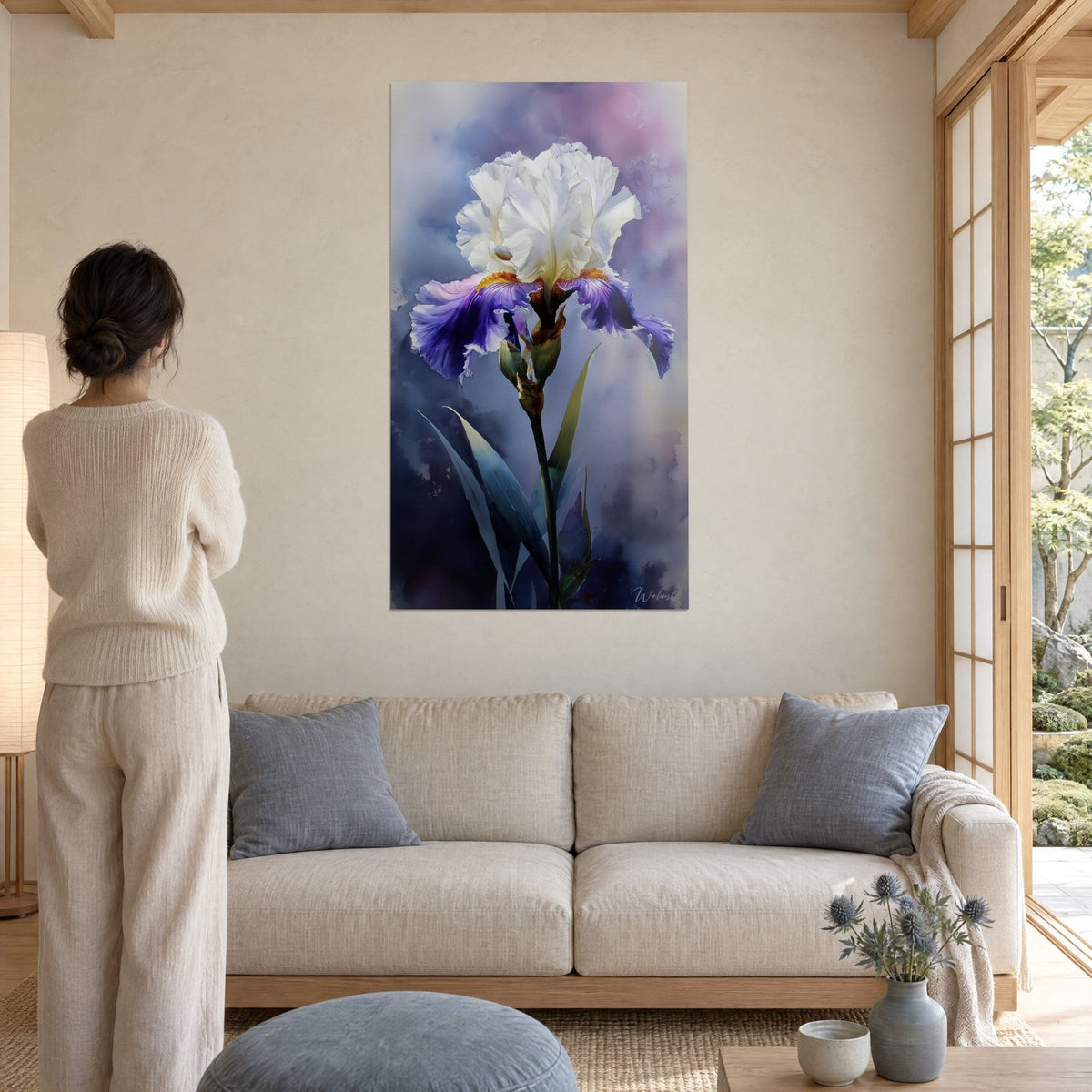 Quadro iris bianco dai petali stropicciati, stami color zafferano e sepali viola, donna di spalle, sopra un divano in un soggiorno luminoso