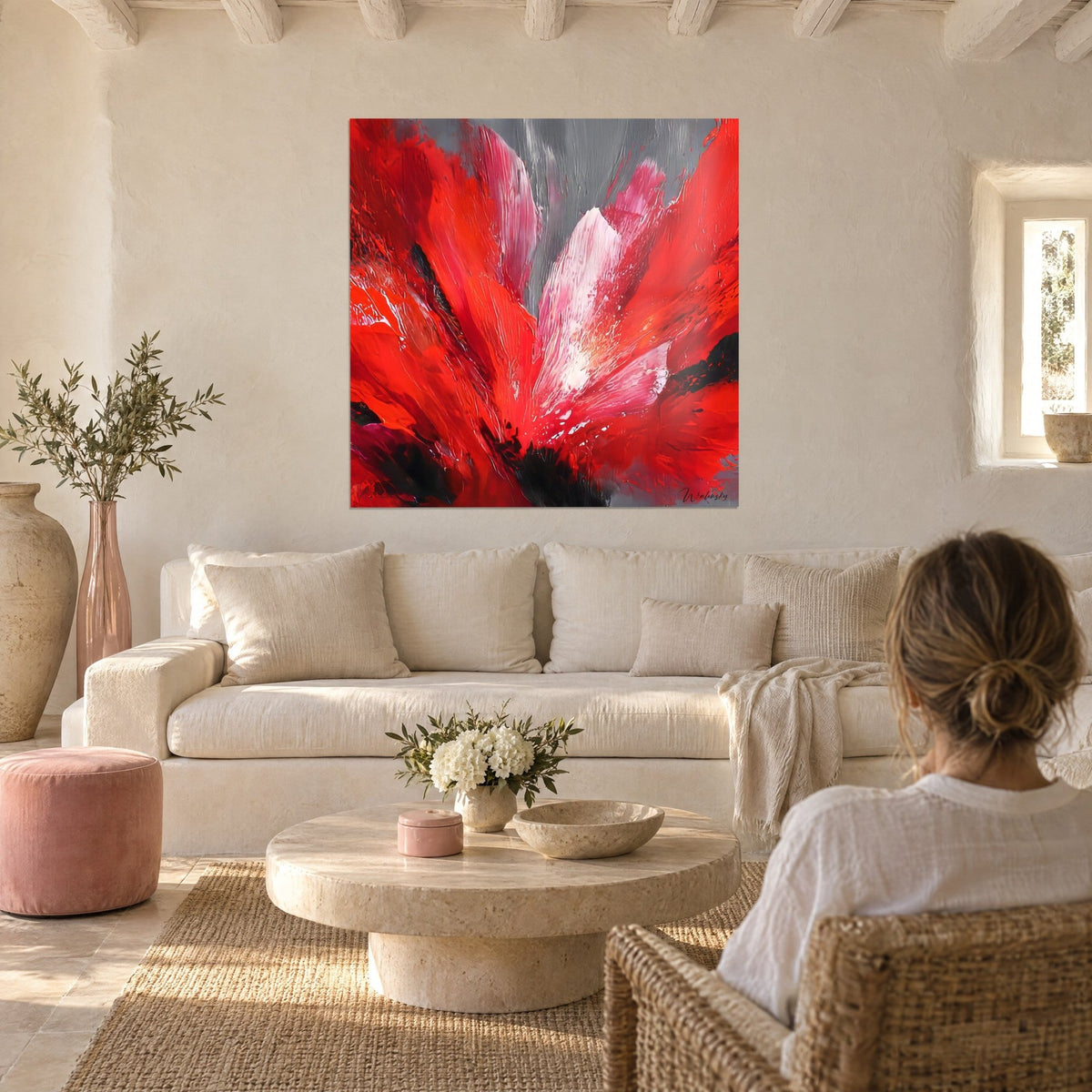 Tableau fleur rouge explosée aux pétales carmin et rose sur fond gris, une femme de dos au-dessus d'un canapé dans un salon lumineux