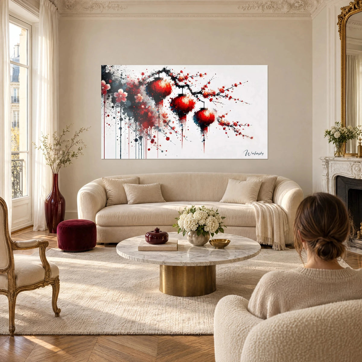 Quadro con lanterne rosse appese a un ramo nero, fiori rosa pallido e colature su fondo bianco, sopra un divano in un soggiorno luminoso