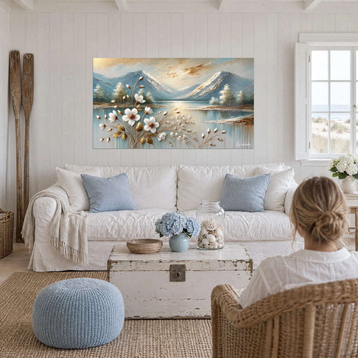 Tableau fleurs blanches au cœur doré devant un lac et des cimes bleues, au-dessus d'un canapé dans un salon lumineux