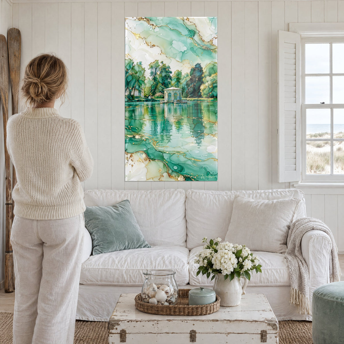 Quadro padiglione bianco sul laghetto, riflessi verde giada e oro, donna di spalle, sopra un divano in un soggiorno luminoso