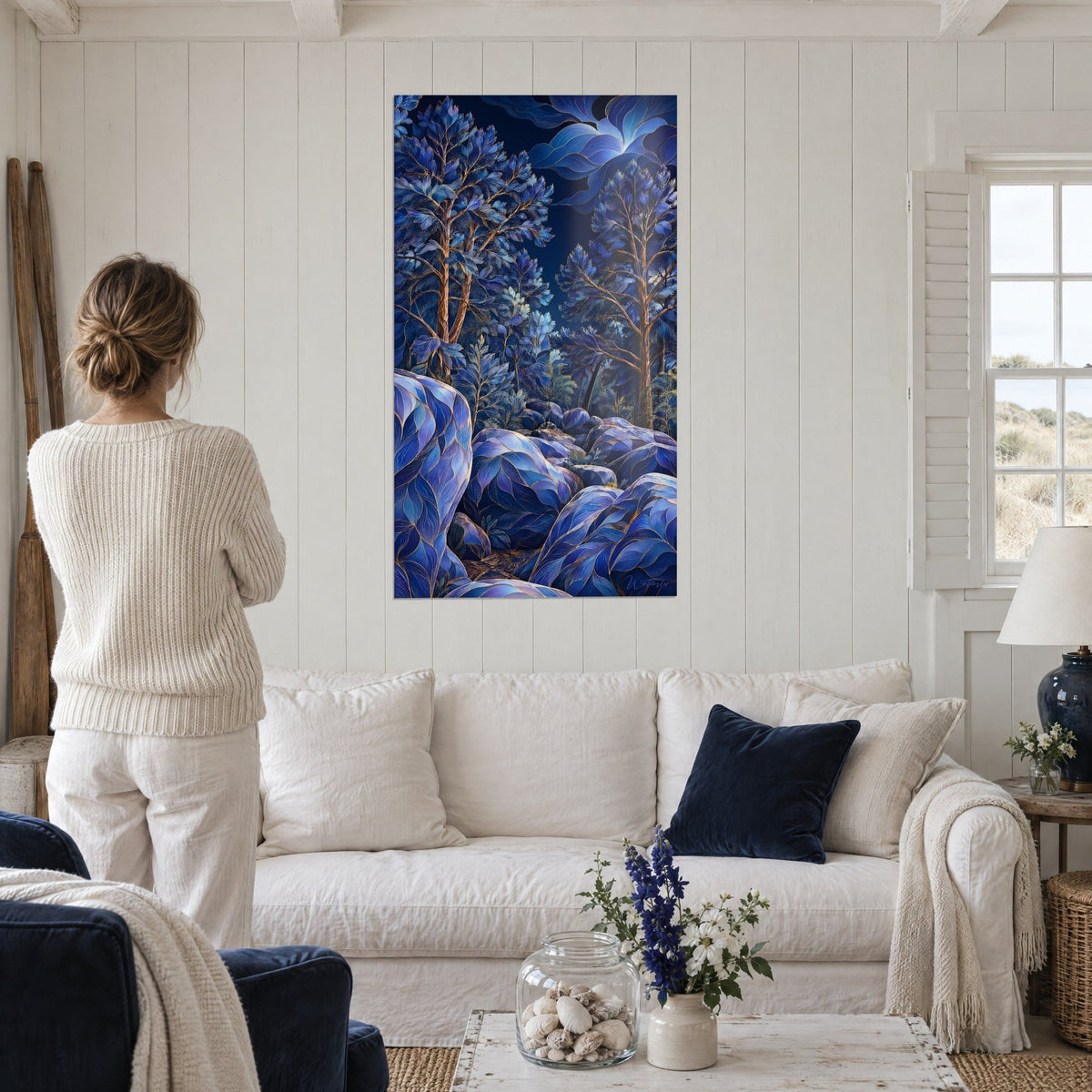 Gemälde Mondwald mit bernsteinfarbenen Kiefern und kobaltblauen, golden geäderten Felsen, Frau von hinten, über einem Sofa in einem hellen Wohnzimmer