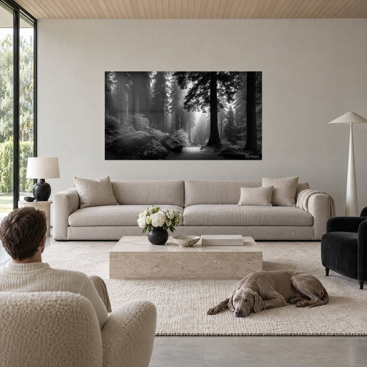 Quadro di un sottobosco nebbioso in bianco e nero, sentiero chiaro tra abeti grigi, sopra un divano in un soggiorno luminoso