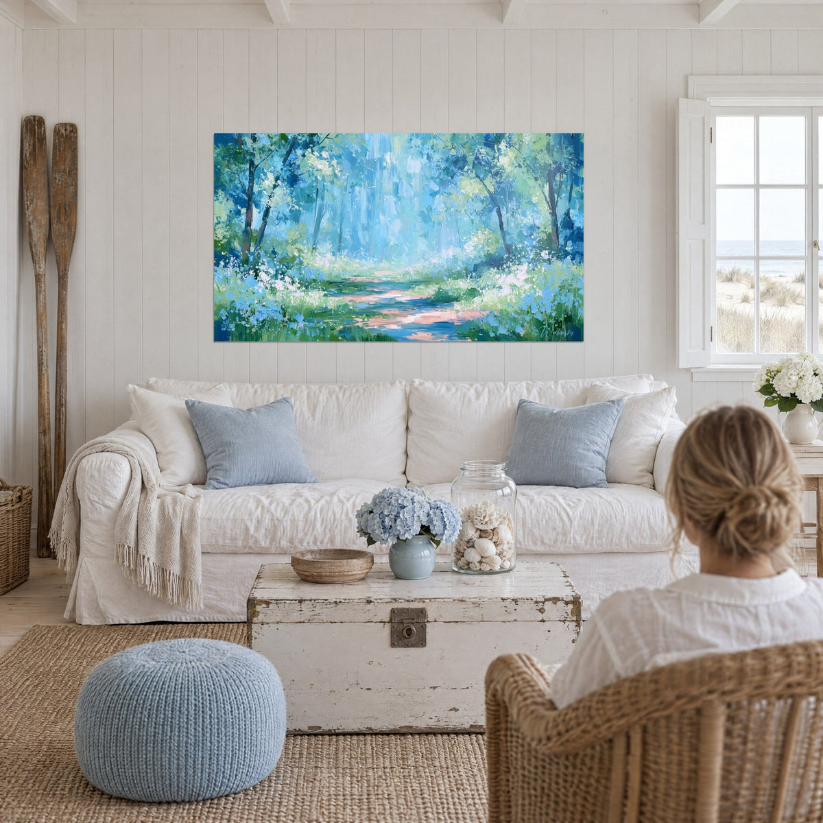 Gemälde eines rosa gepuderten Pfades, der sich durch einen blau-grünen Wald schlängelt, über einem Sofa in einem hellen Wohnzimmer