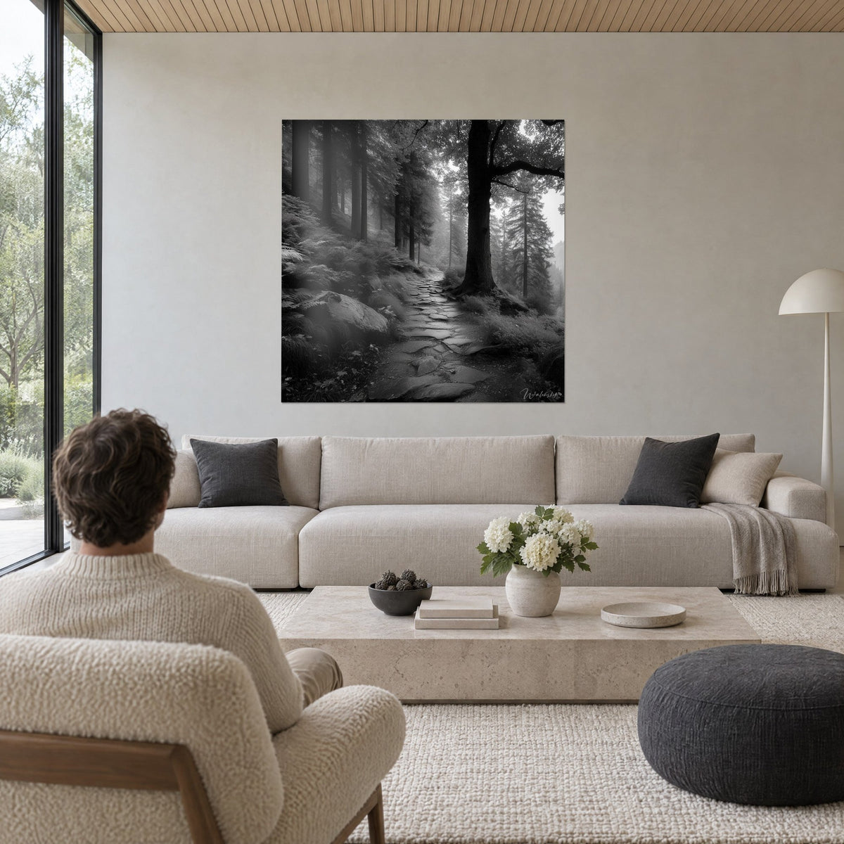 Gemälde Steinplattenpfad durch einen nebligen Wald, Schwarzweiß, hohe graue Tannen, beiges Sofa, helles Wohnzimmer