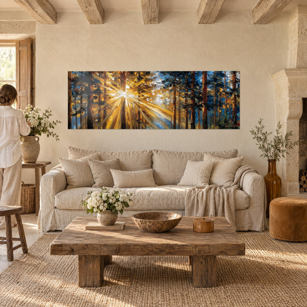 Wall art pine forest burst open by golden sunlight, russet trunks and blue sky, above a sofa in a bright living room