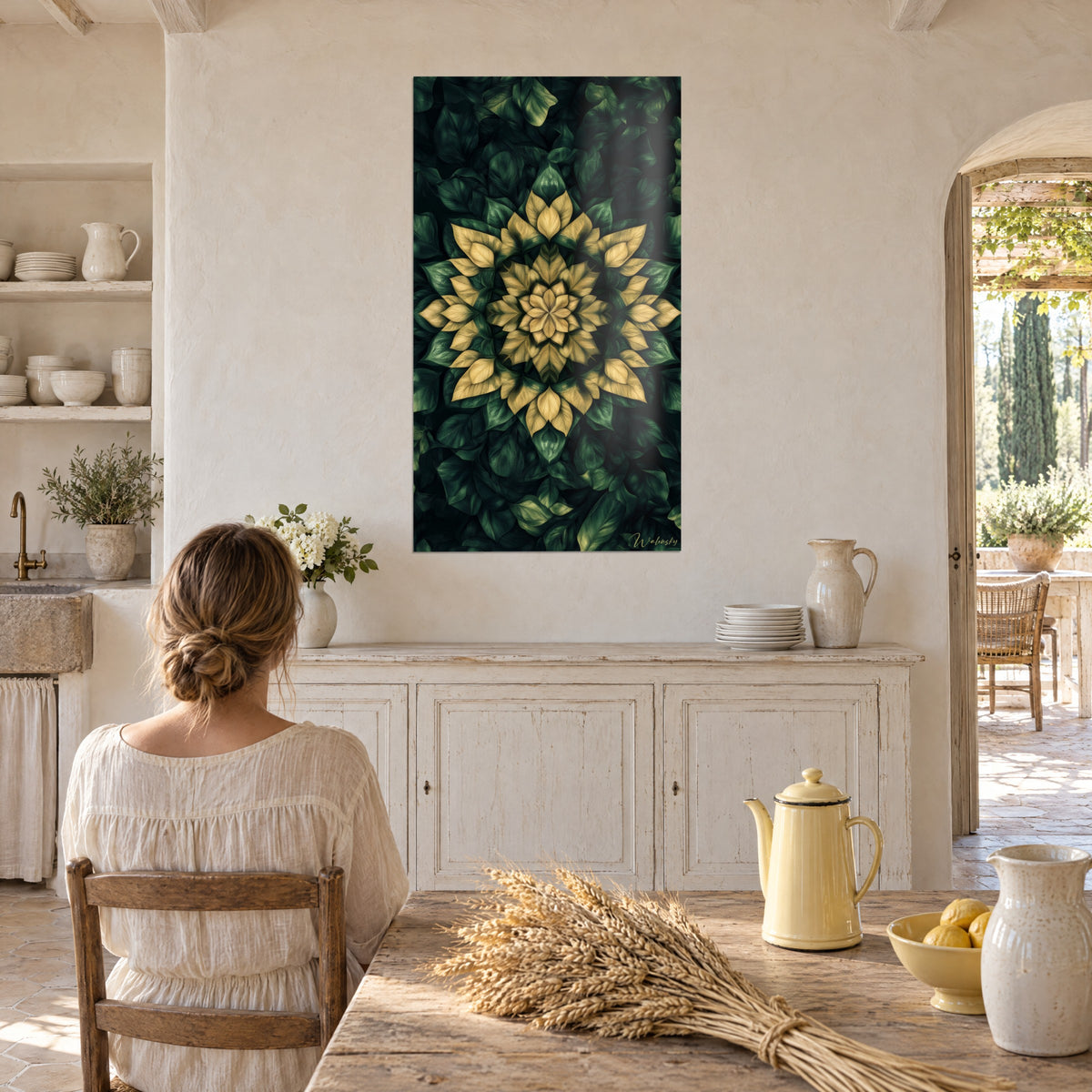 Cuadro motivo floral simétrico amarillo arena y verde profundo, cocina de piedra clara, mujer de espaldas sentada a la mesa junto a cerámicas