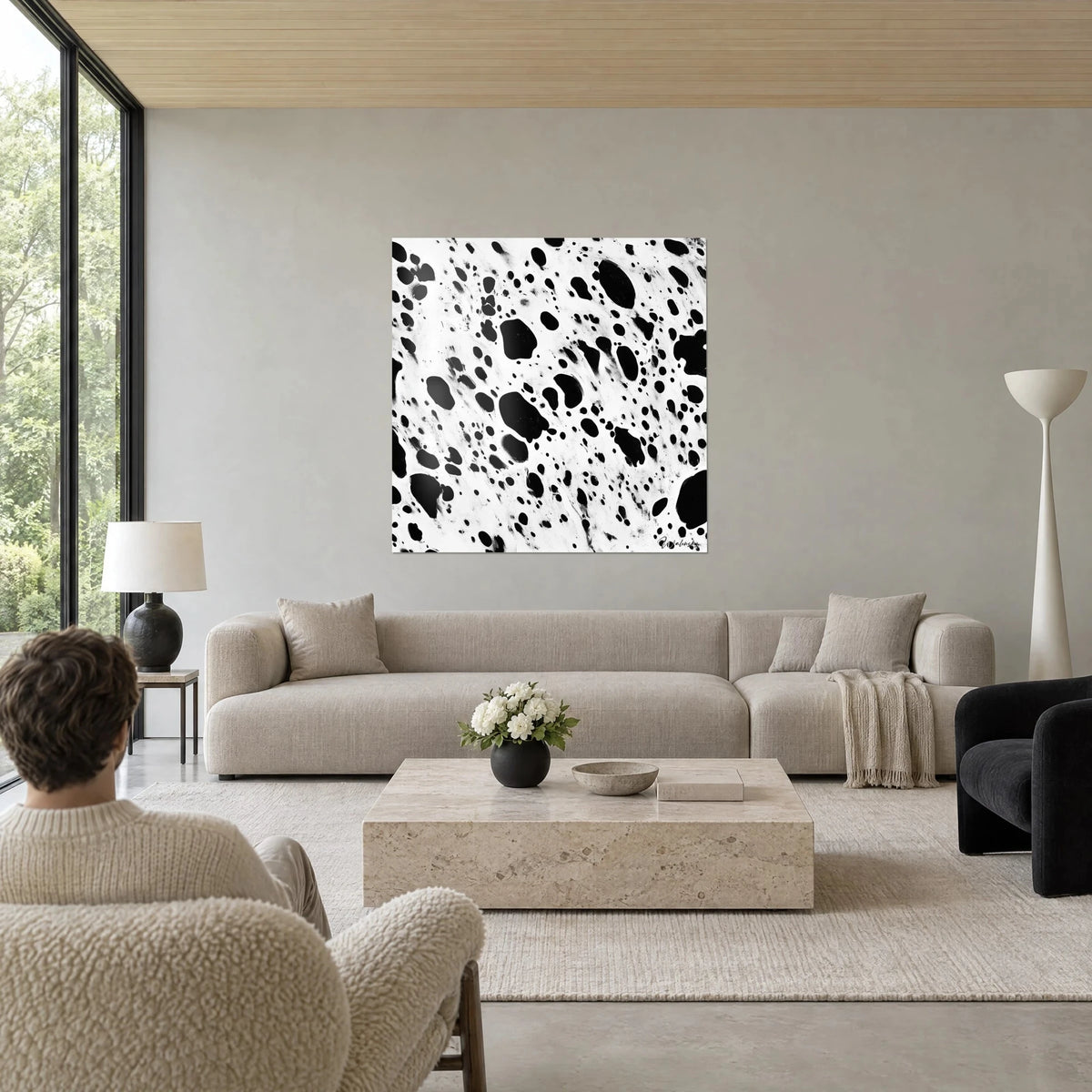 Tableau taches d'encre noire éclaboussées sur fond blanc, deux personnes de dos, au-dessus d'un canapé dans un salon lumineux