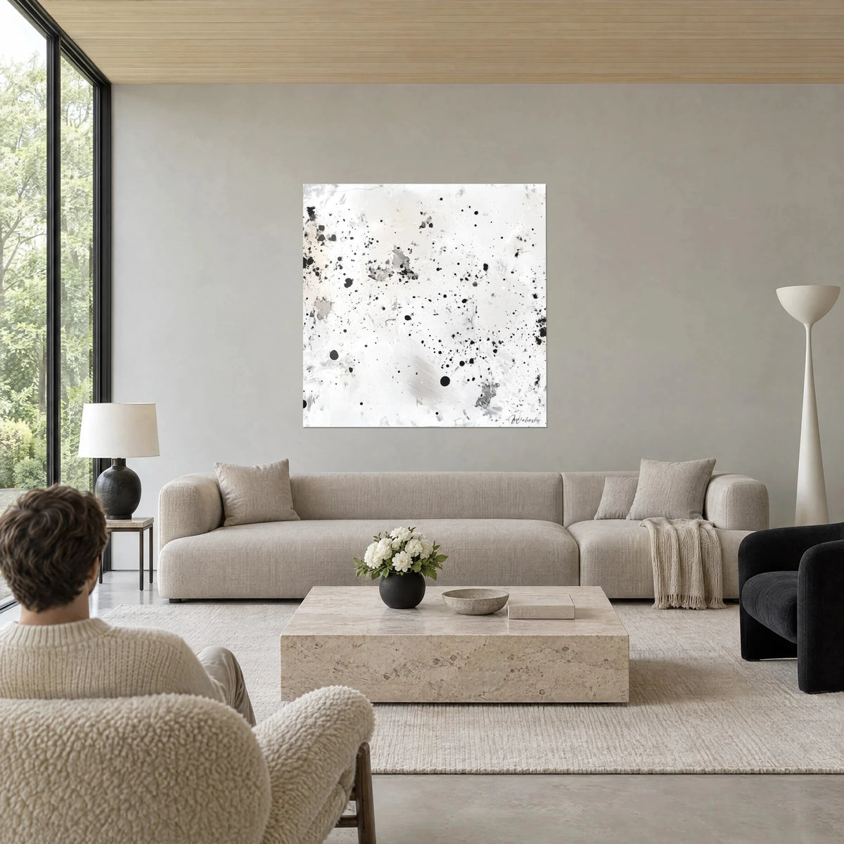 Cuadro con salpicaduras de tinta negra sobre fondo blanco crema y gris perla, una persona de espaldas, sobre un sofá en un salón luminoso