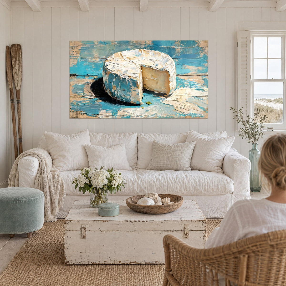 Tableau camembert entier à la croûte blanche, part retirée et ombre noire sur planches turquoise, au-dessus d'un canapé dans un salon lumineux