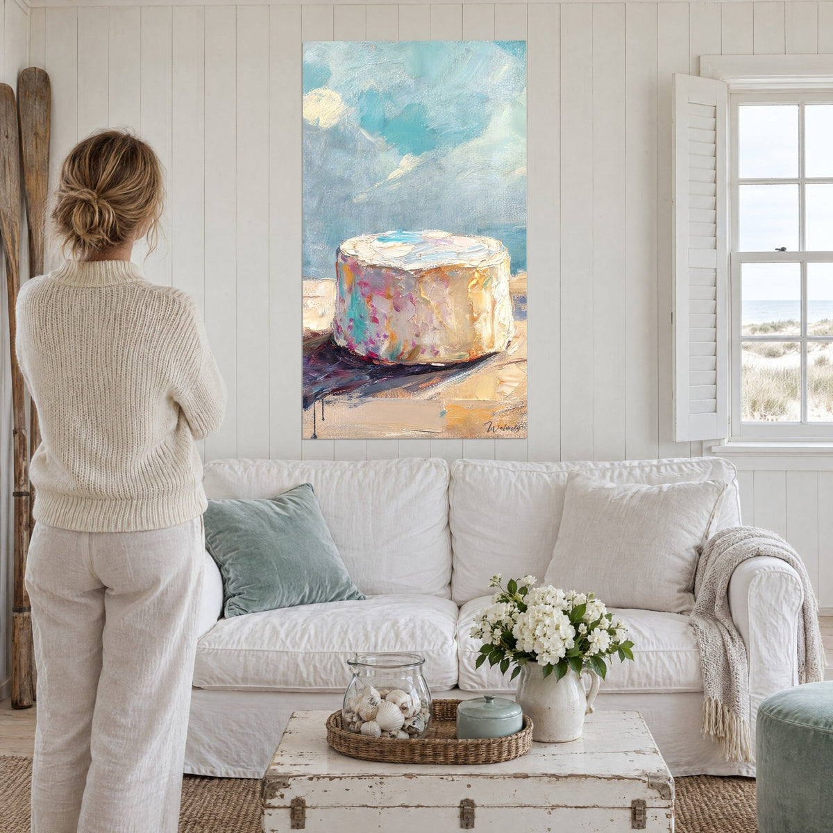 Tableau fromage rond crème aux éclats rose et turquoise sur ciel bleu, empâtements épais, au-dessus d'un canapé dans un salon lumineux