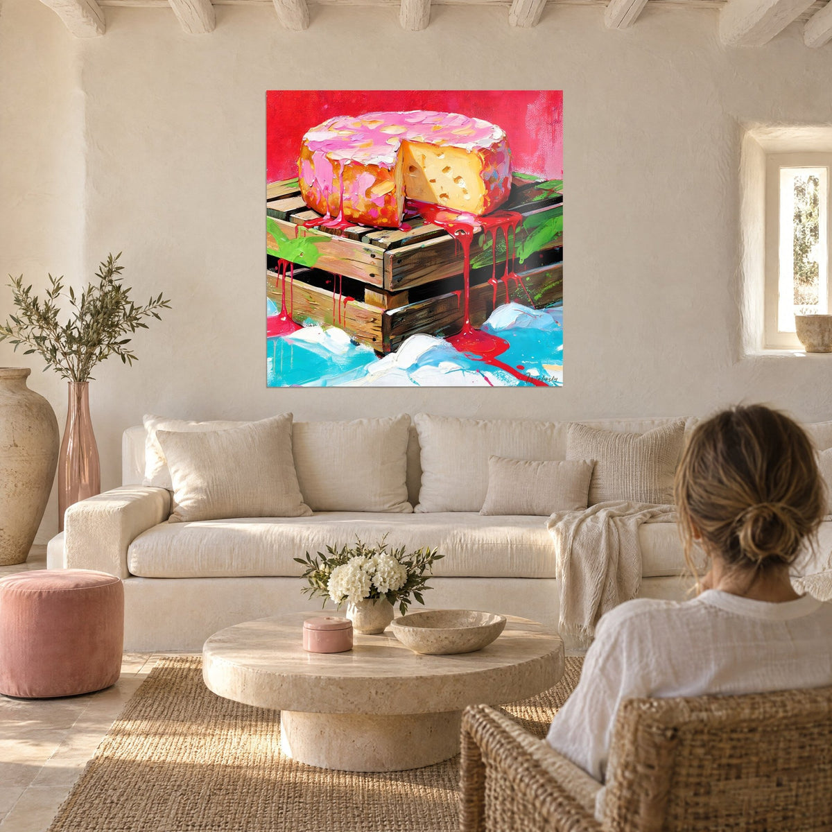 Tableau meule de fromage nappée de rose, coulures rouges sur caisse en bois, femme de dos, au-dessus d'un canapé dans un salon lumineux