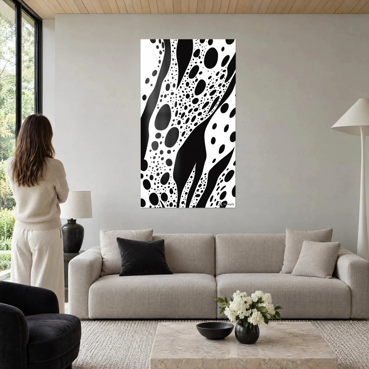 Quadro di volute nere su fondo bianco, nuvole di pois, donna di spalle sopra un divano in un soggiorno luminoso