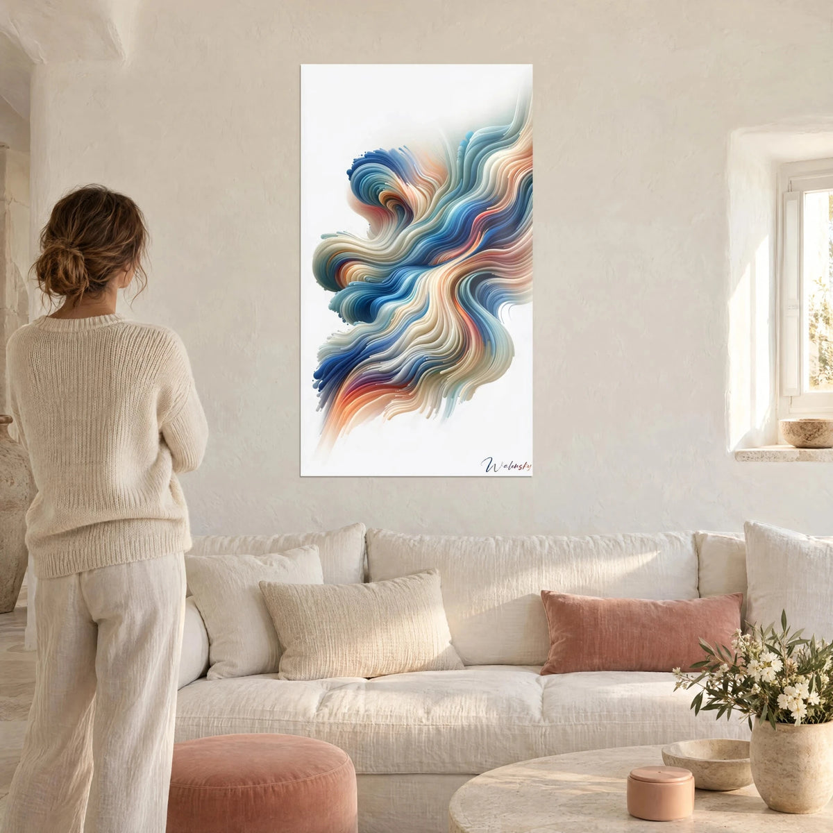 Schilderij met vloeiende golven in kobaltblauw en koraal op witte achtergrond, vrouw van achteren in crèmekleurige trui, boven een bank in een lichte woonkamer