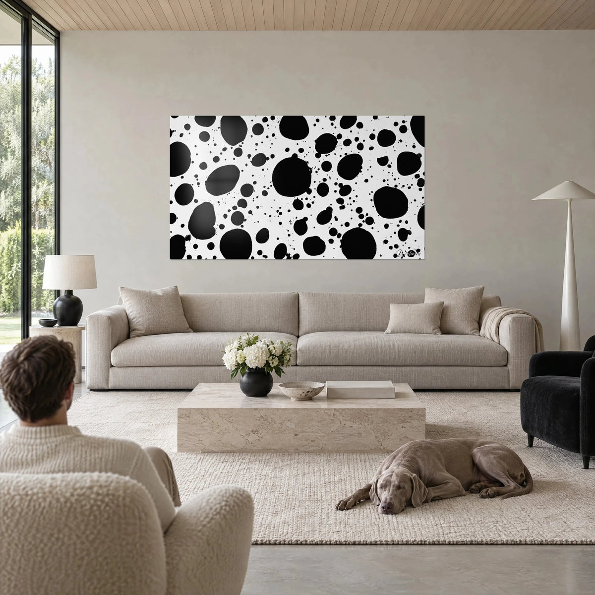 Gemälde mit schwarzen Tintenspritzern auf weißem Grund, große und kleine Tropfen, über einem Sofa in einem hellen Wohnzimmer