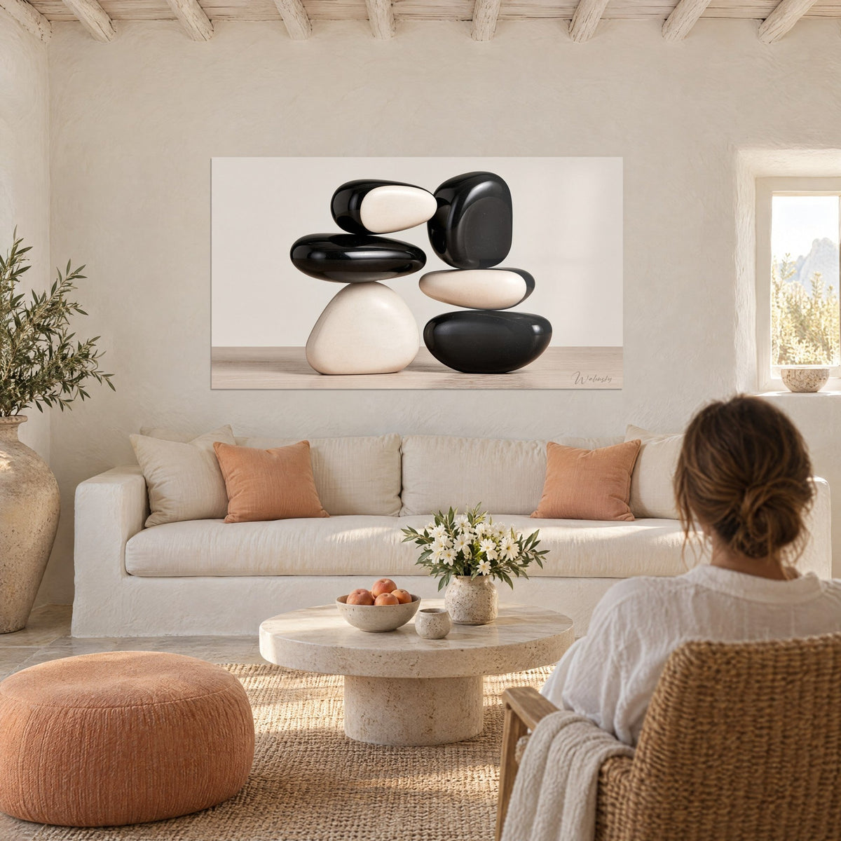 Cuadro guijarros apilados en blanco y negro en equilibrio, lacados y crema, sobre un sofá en un salón luminoso