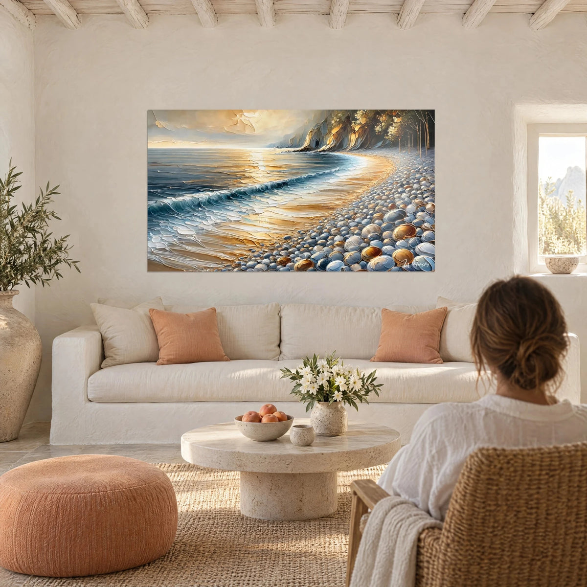 Wall art of pebbled shore in bluish stones under golden sun, turquoise wave and ochre cliff, above a sofa in a bright living room