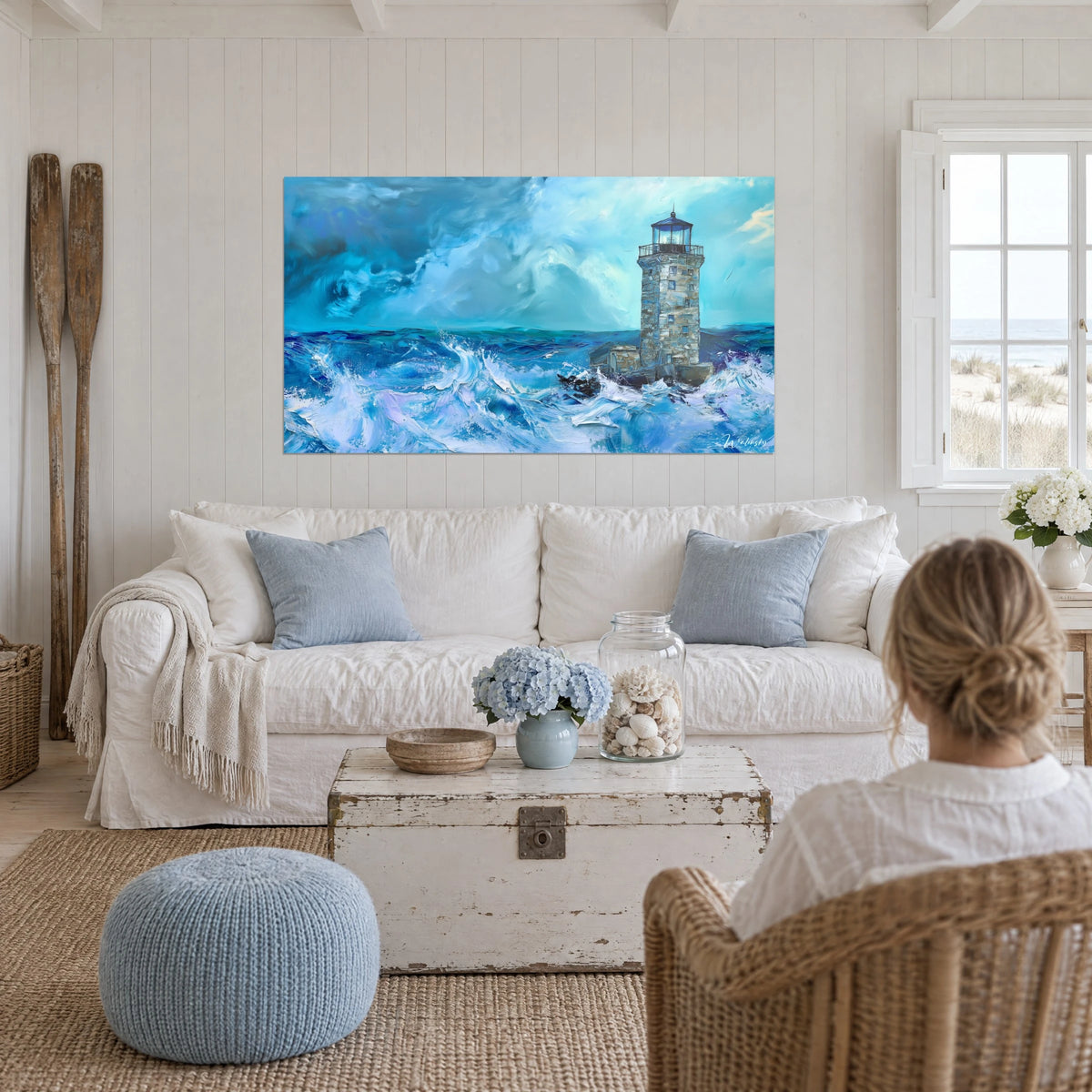 Tableau phare de pierre sous orage, vagues bleu cobalt et écume blanche, femme de dos au-dessus d'un canapé dans un salon lumineux