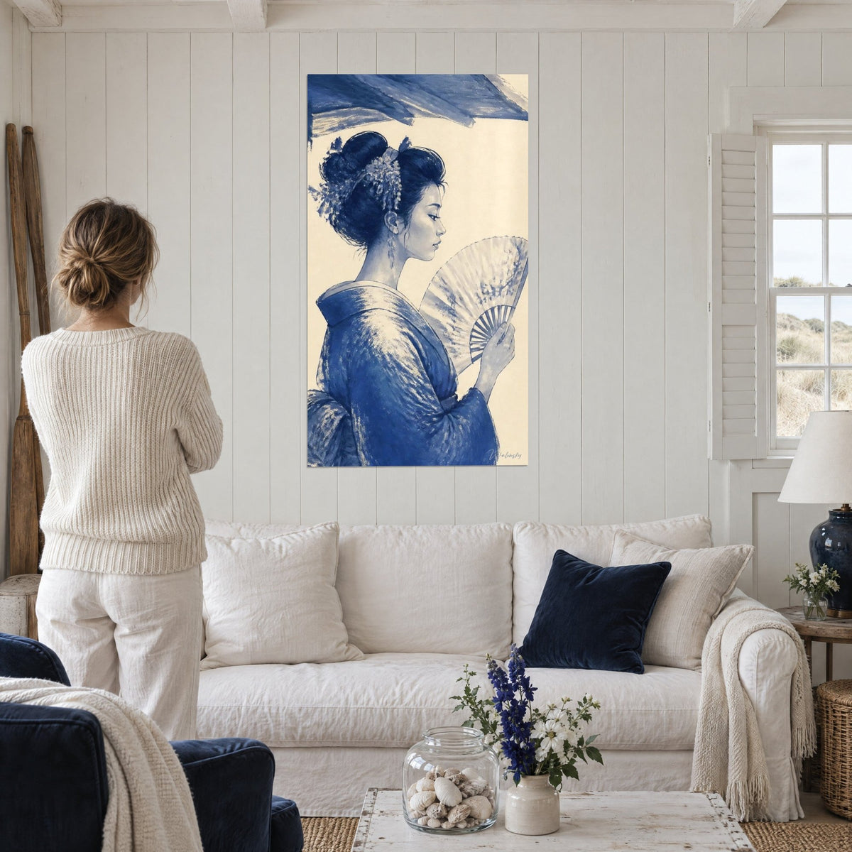 Tableau geisha de profil au kimono indigo, éventail ajouré sur fond crème, au-dessus d'un canapé dans un salon lumineux