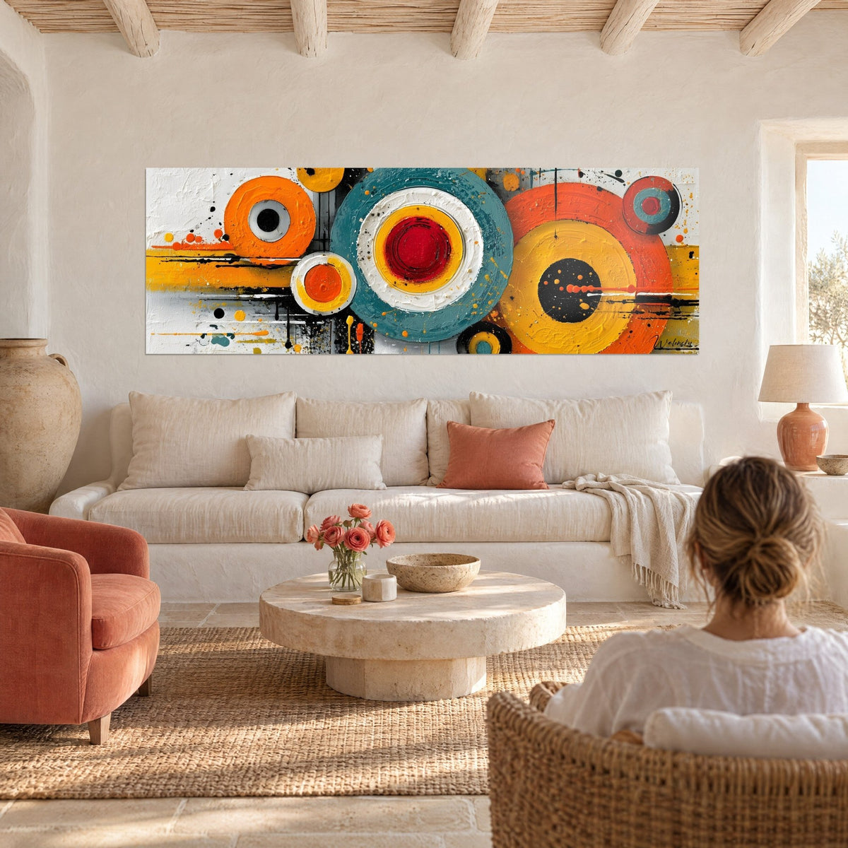 Cuadro círculos concéntricos naranja y verde azulado, corazón rojo sobre fondo blanco, con una mujer de espaldas, sobre un sofá en un salón luminoso
