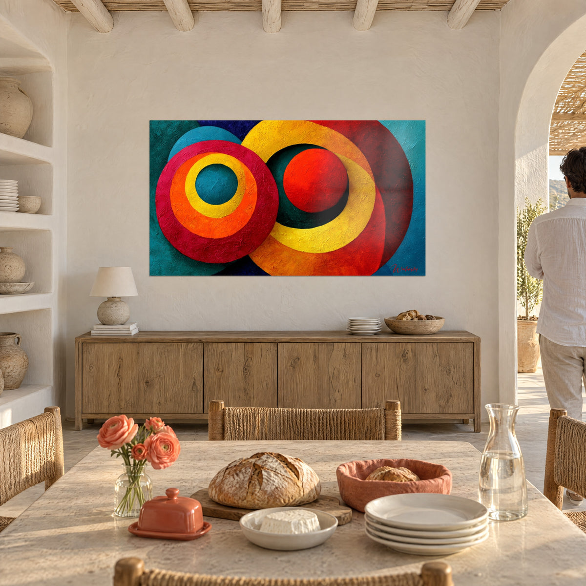Tableau anneaux jaune moutarde et pourpre autour d'une boule vermillon, mur chaulé, table en bois, personne de dos dans l'arche