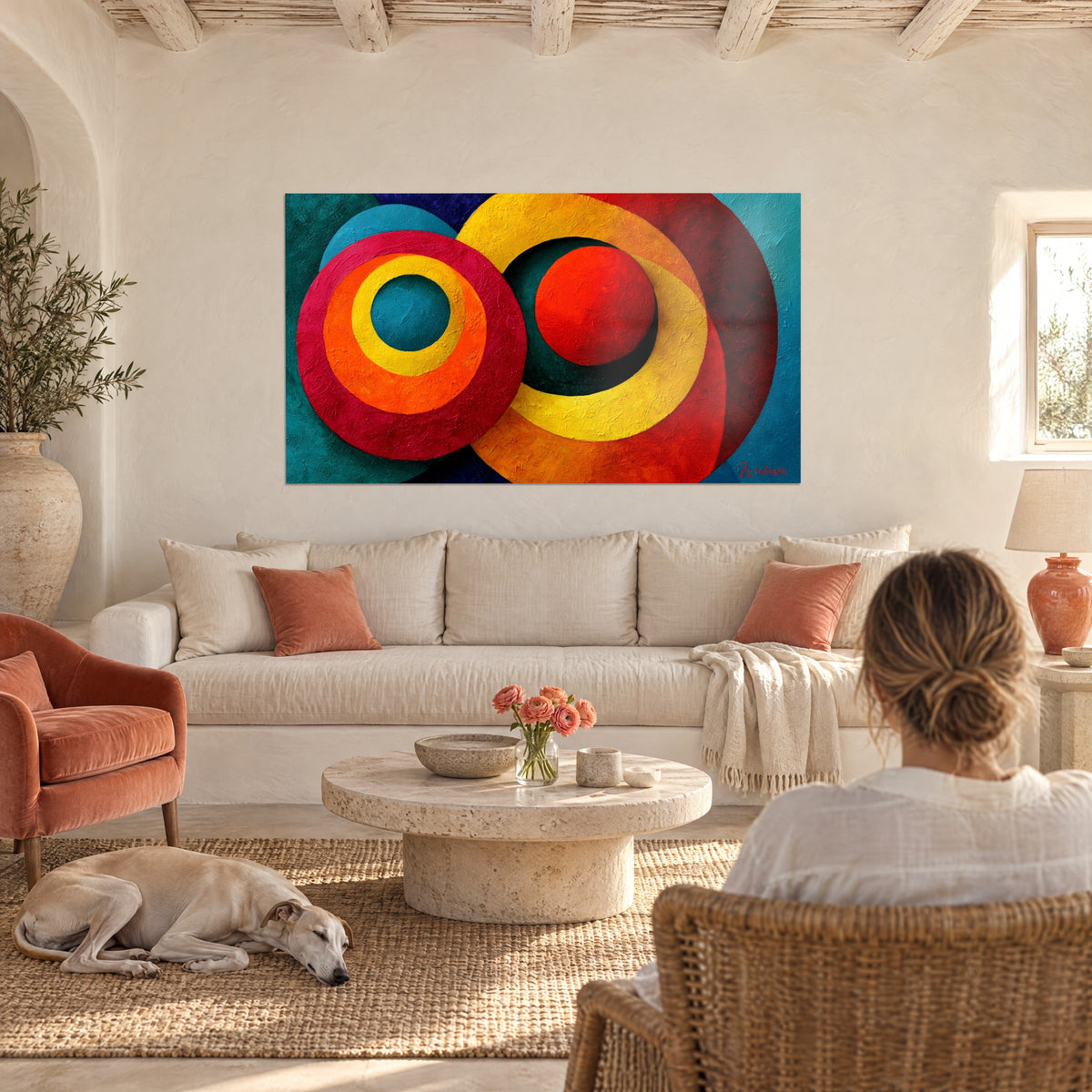 Tableau cercles concentriques carmin et jaune citron sur fond sarcelle, personne de dos et lévrier, au-dessus d'un canapé dans un salon lumineux