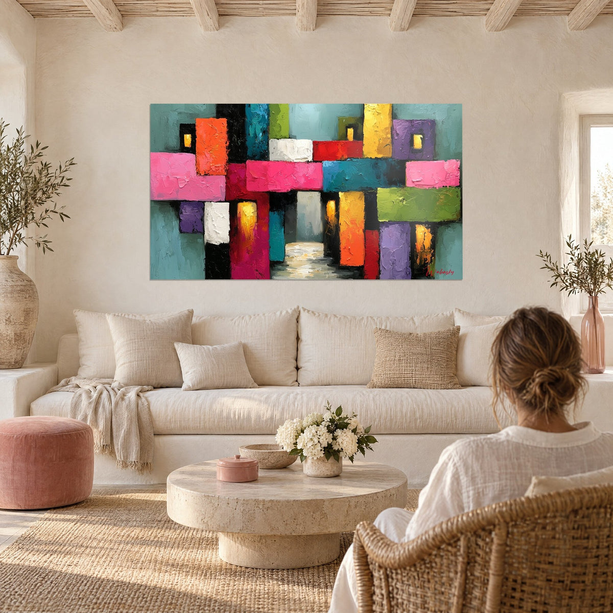 Tableau ruelle colorée aux blocs roses et turquoise, passage lumineux ocre, personne de dos au-dessus d'un canapé dans un salon lumineux