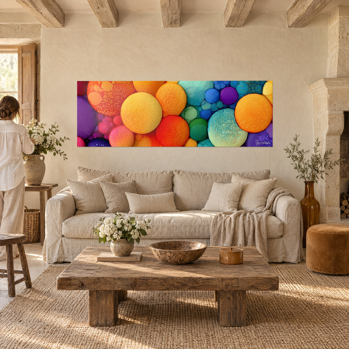 Schilderij met reusachtige oranje en turquoise bellen in reliëf, een vrouw van achteren op de voorgrond, boven een bank in een lichte woonkamer