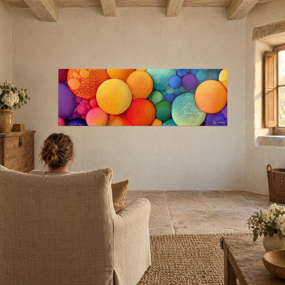 Schilderij met abstracte turquoise, oranje en violette planeten, een vrouw van achteren in een beige fauteuil, woonkamer met zichtbare balken