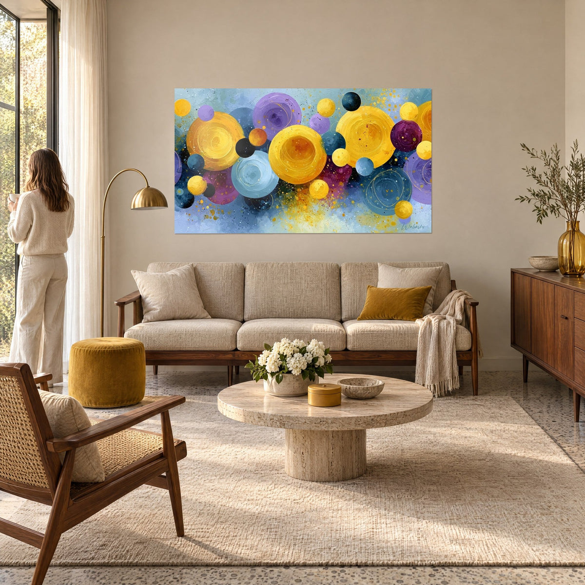 Gemälde mit goldenen und violetten Kugeln in Splittern, sonnengelb und himmelblau, Frau von hinten, über einem Sofa in einem hellen Wohnzimmer
