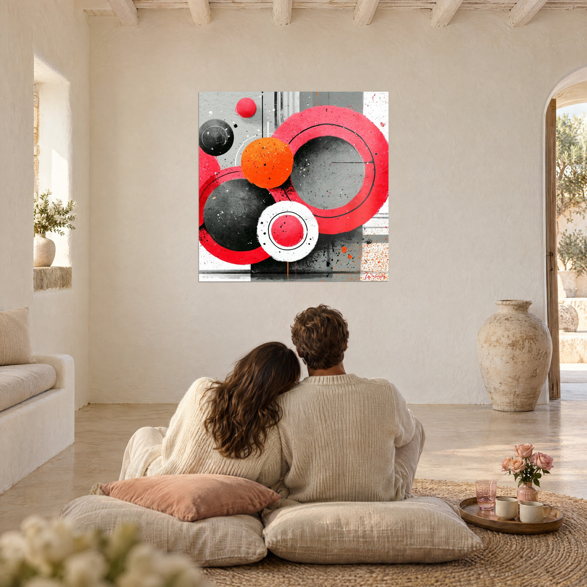 Tableau ronds rouge vif et noir mat éclaboussés d'orange, un couple de dos assis sur des coussins dans un salon blanc