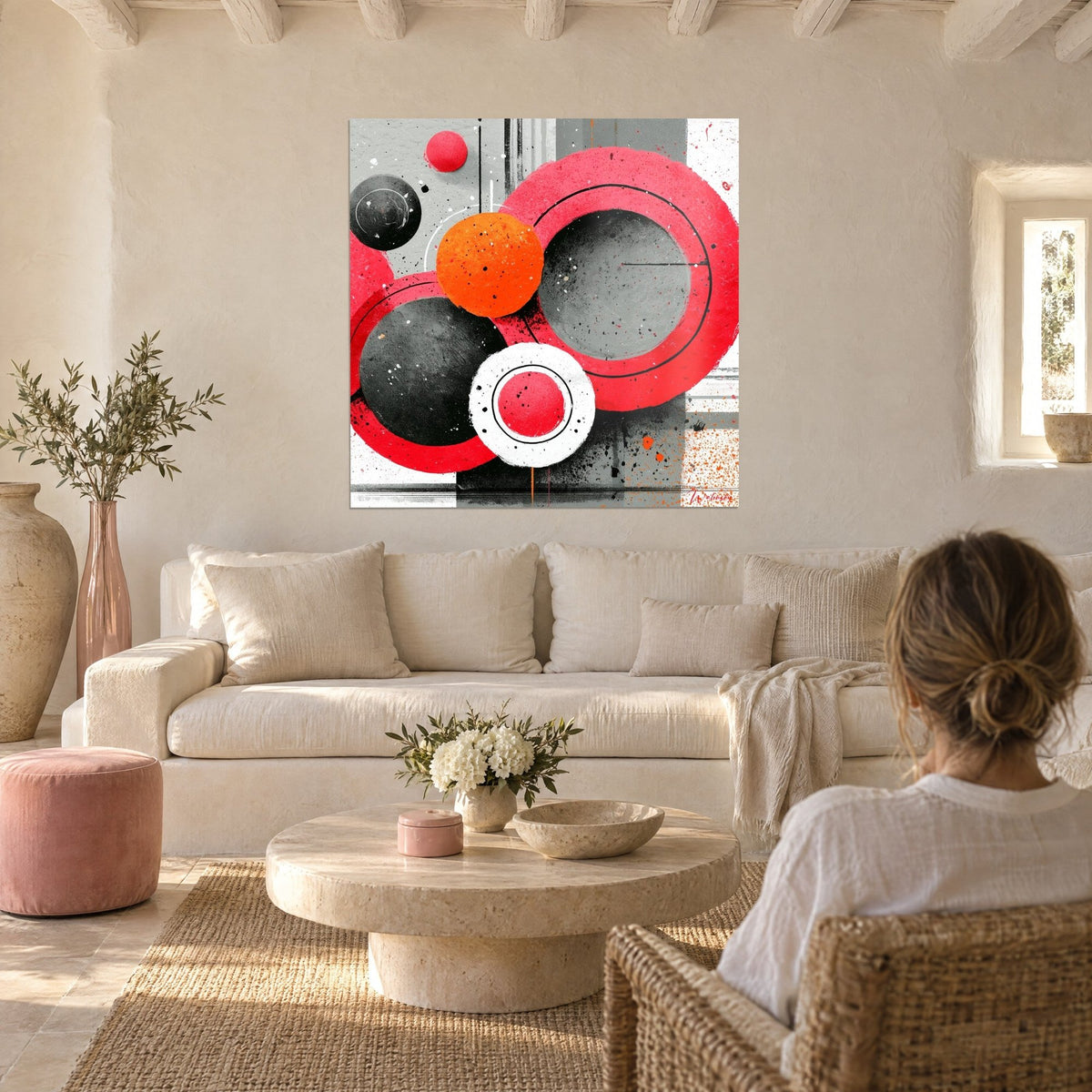 Quadro cerchi rosso lampone cerchiati di nero e una sfera arancione, una donna di spalle sopra un divano in un soggiorno luminoso