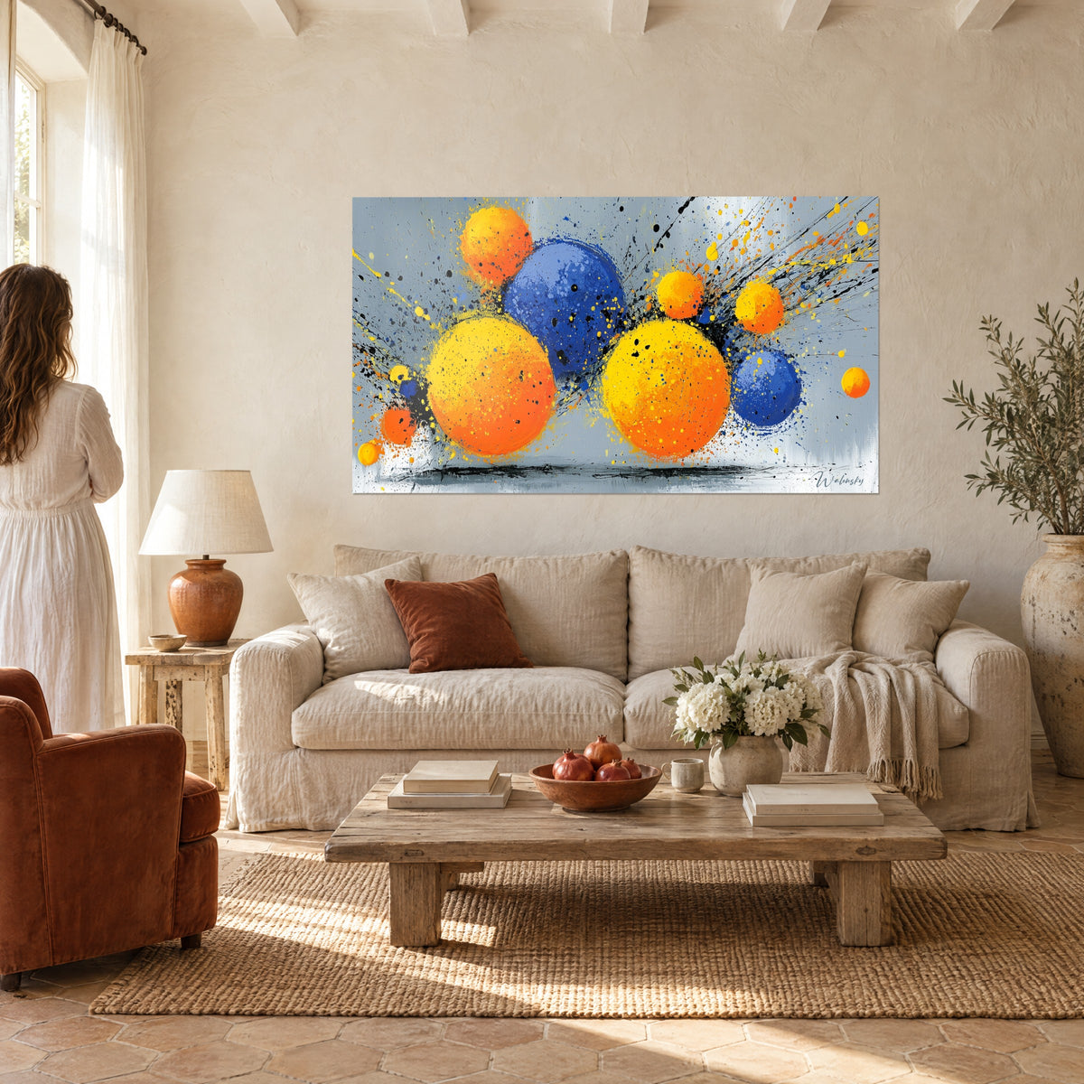 Tableau sphères orange et bleu cobalt éclaboussées d'encre noire, femme de dos en robe blanche, au-dessus d'un canapé dans un salon lumineux