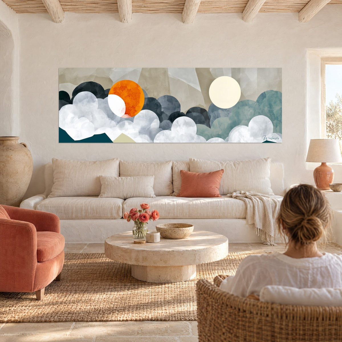 Wall art double sun in orange and cream over navy blue clouds, woman seen from behind, above a sofa in a bright living room