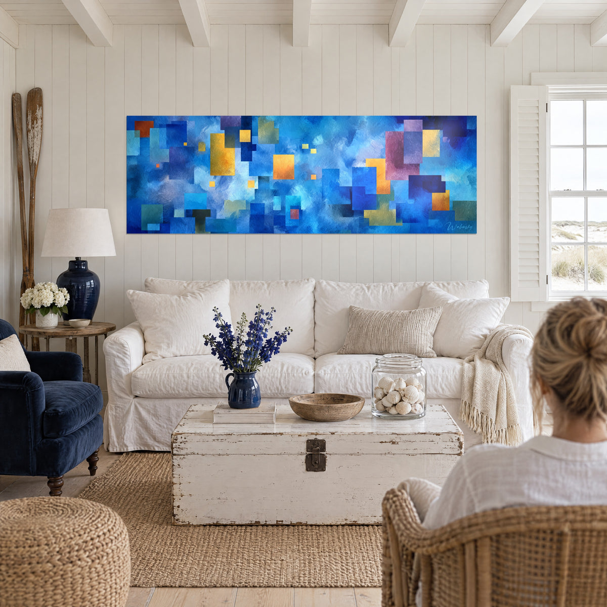 Gemälde Mosaik aus kobaltblauen und ockergelben Quadraten, zwei Personen von hinten, über einem Sofa in einem hellen Wohnzimmer