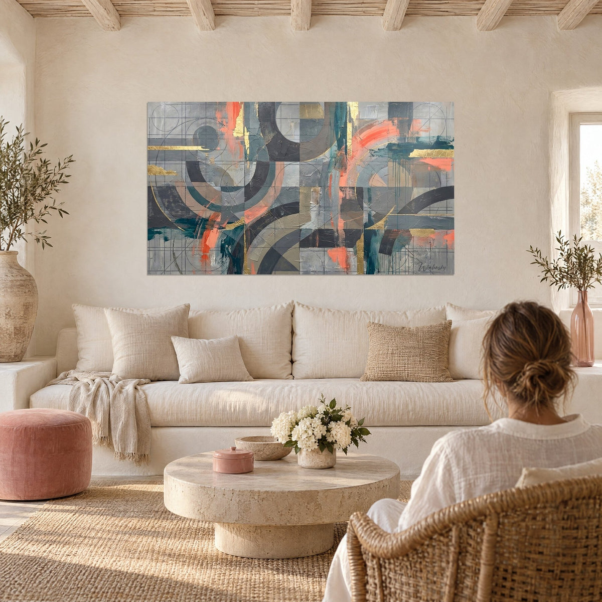 Quadro con archi geometrici grigio ardesia e corallo, tocchi d'oro, griglia sottile, una donna di spalle, sopra un divano in un soggiorno luminoso