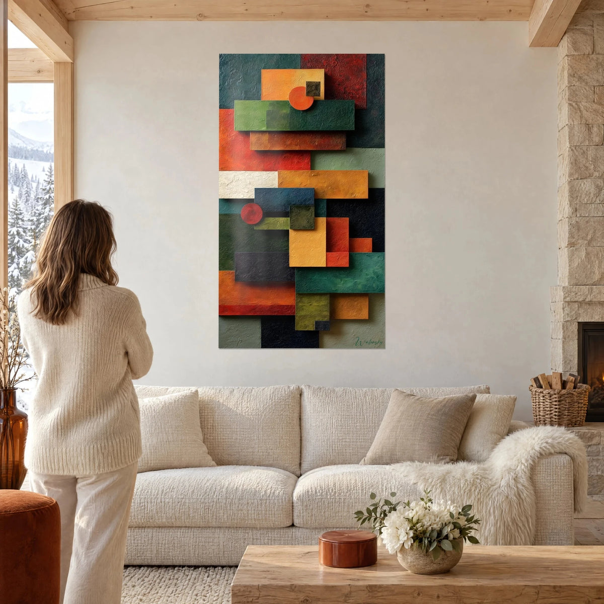 Tableau composition géométrique de rectangles orange, vert sapin et rouge brique, femme de dos, au-dessus d'un canapé dans un salon lumineux