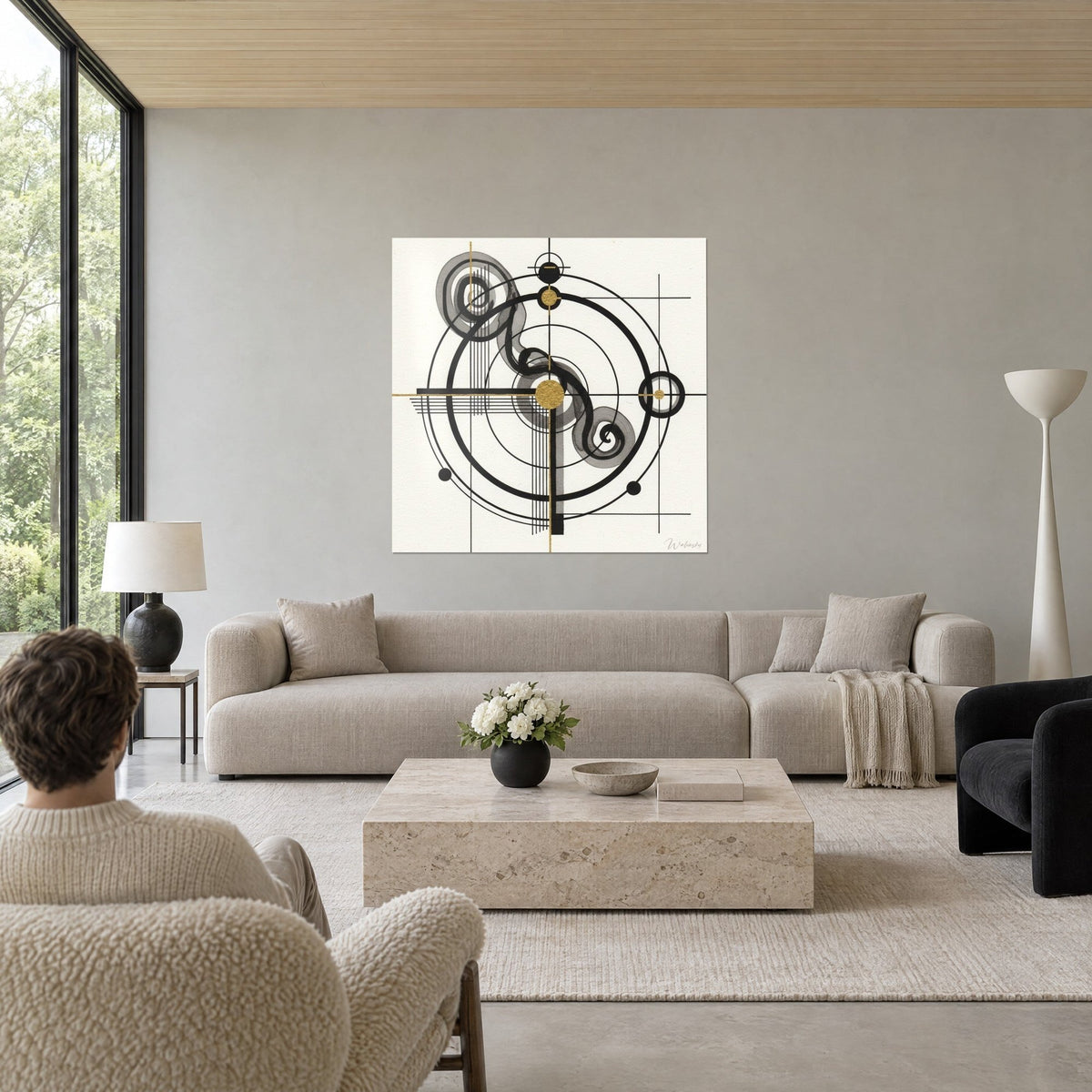 Wall art with black concentric circles, a gold dot and grey ink spirals, person seen from behind, above a sofa in a bright living room