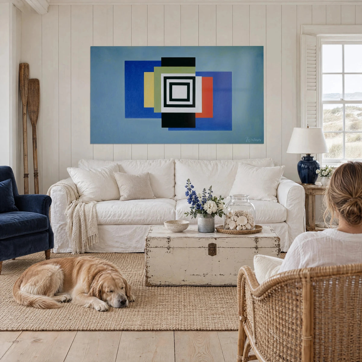 Wall art black and white concentric squares on sky blue background, hung above a sofa in a bright living room