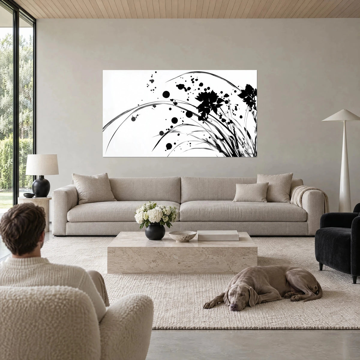 Wall art of arched black grass sheaves on a white background, ink splatters, beige and grey, above a sofa in a bright living room