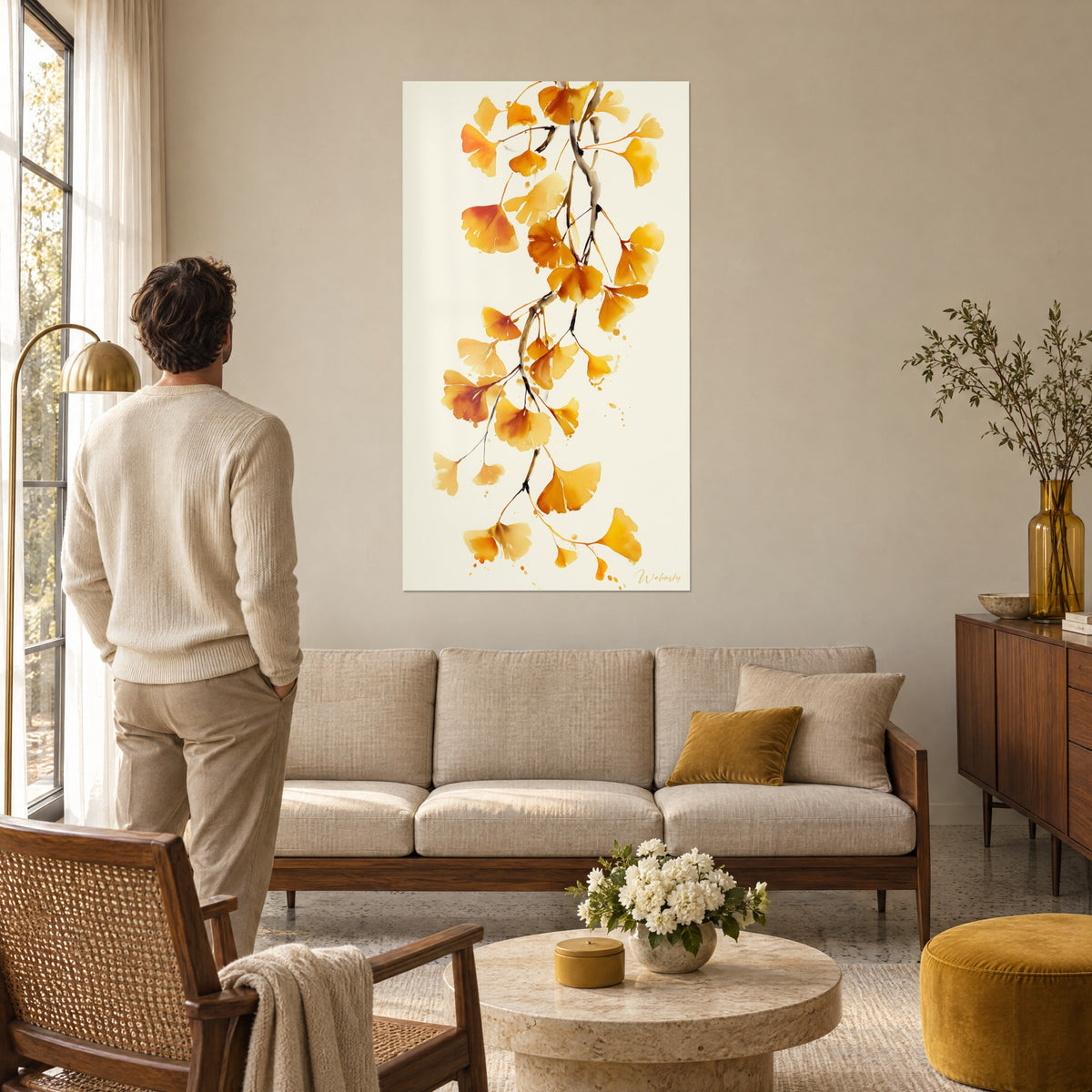 Schilderij gouden ginkgobladeren in aquarel op crème achtergrond, man met de rug naar de kijker, boven een bank in een lichte woonkamer