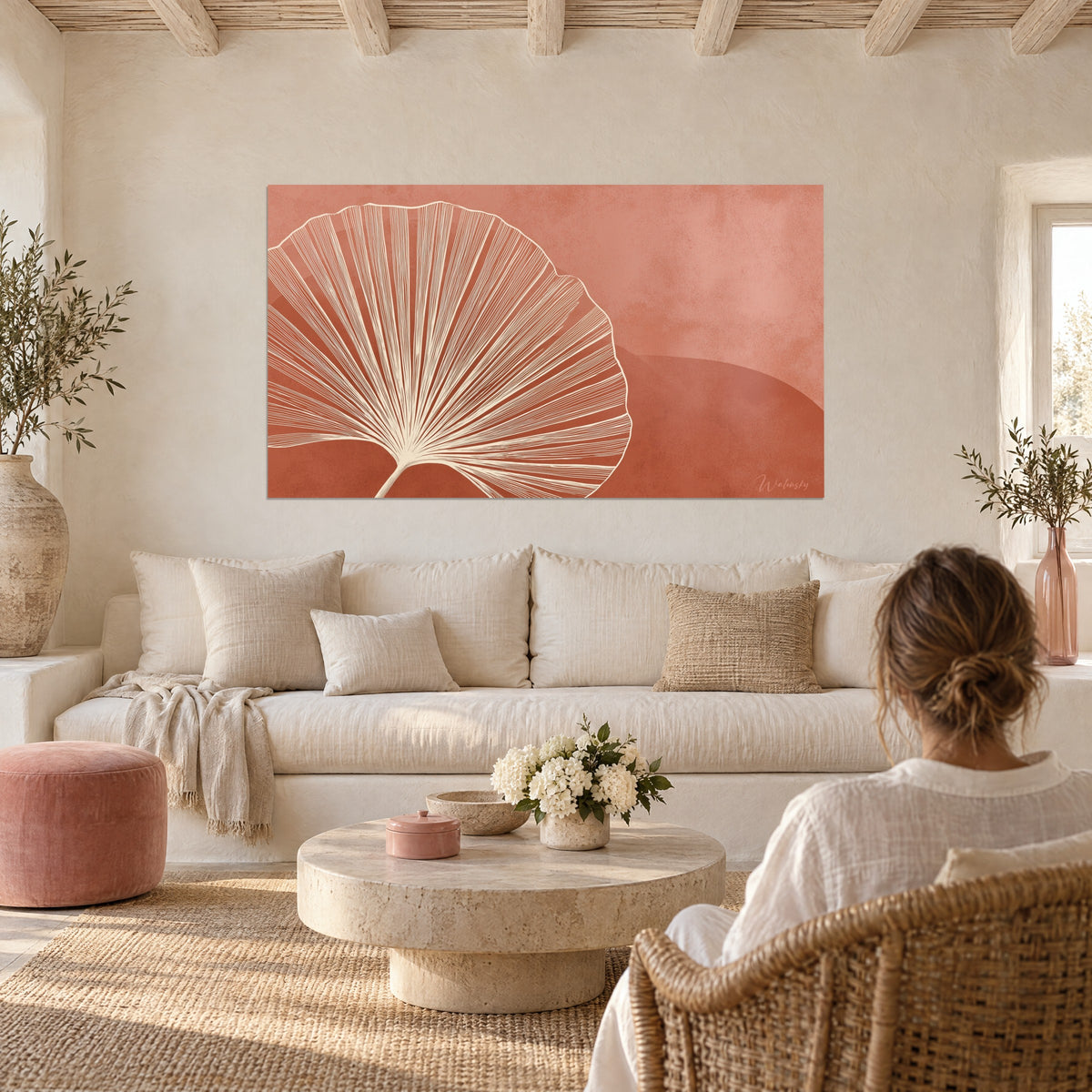 Cuadro hoja de ginkgo en abanico con nervaduras crema sobre fondo terracota, pareja de espaldas, encima de un sofá en un salón luminoso