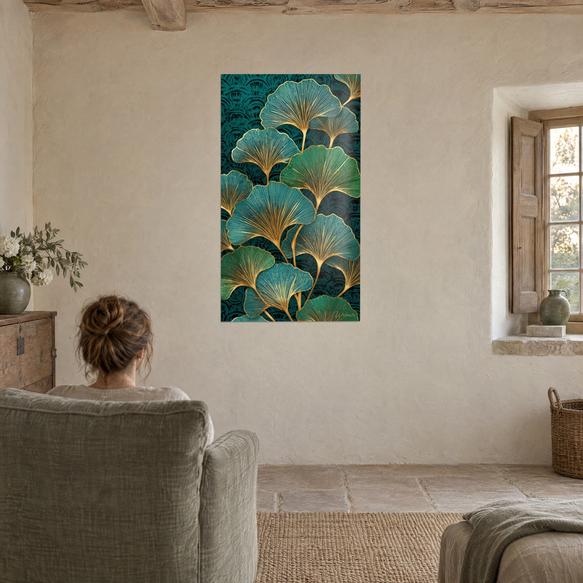 Cuadro hojas de ginkgo esmeralda y turquesa perfiladas en oro, sobre una pared crema, frente a una persona sentada en un sillón