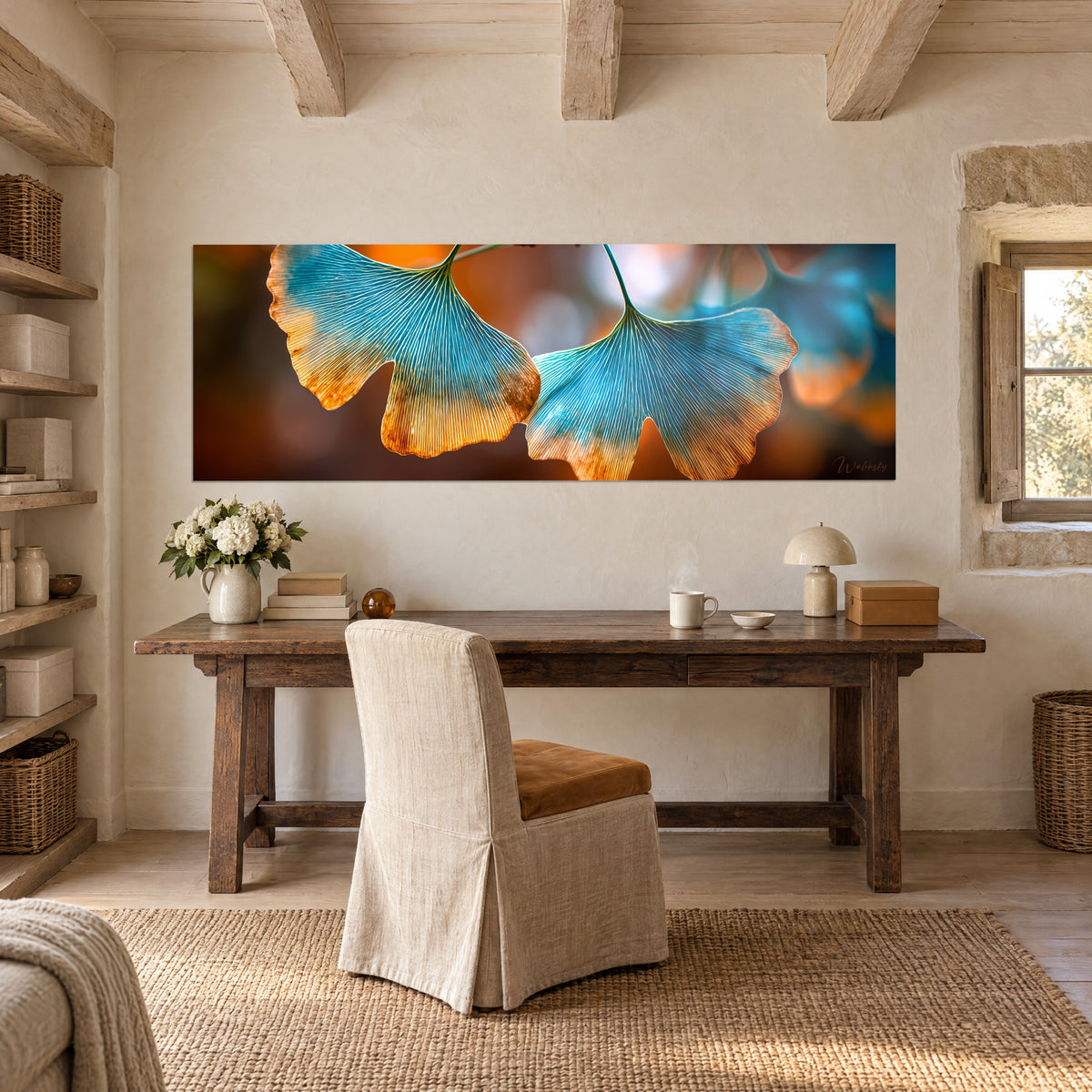 Quadro ramo di ginkgo in controluce, lamine turchesi bordate di arancio e miele, sfondo marrone sfocato, sopra una scrivania in legno