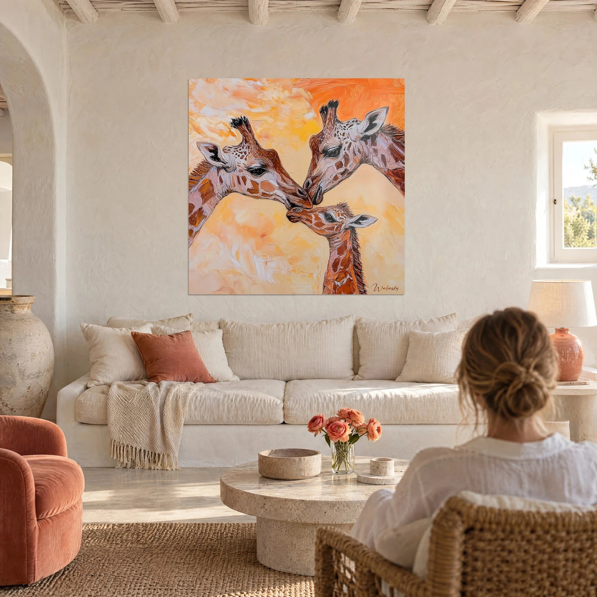 Wall art three giraffes with brown and white coats, orange and yellow background, seen from behind above a sofa in a bright living room