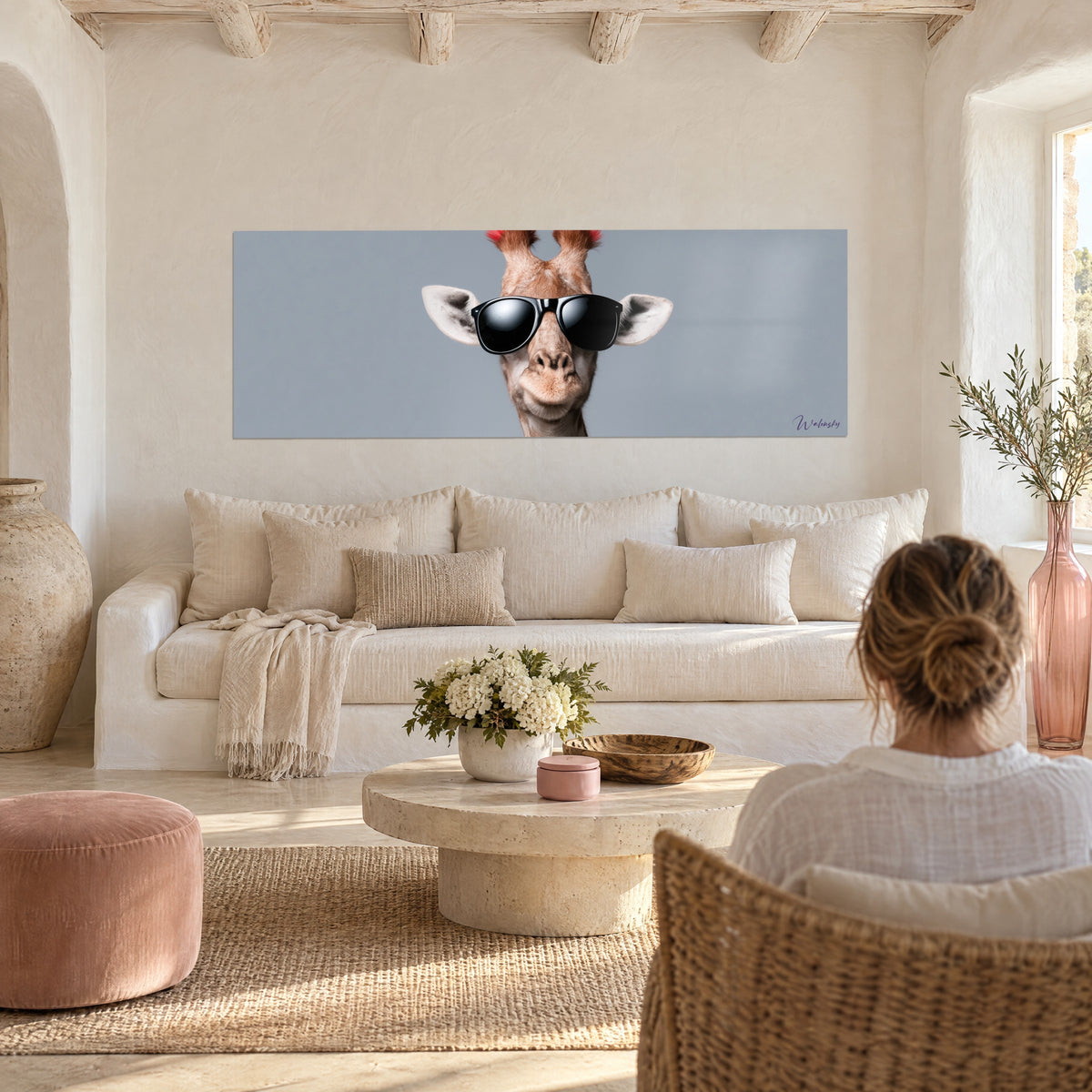 Tableau girafe à lunettes noires, museau beige et fond gris-bleu, une femme de dos au-dessus d'un canapé dans un salon lumineux
